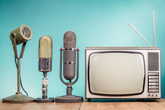 Retro old TV receiver and press conference microphones on table front gradient mint green wall background. Broadcasting concept. Vintage style filtered photo