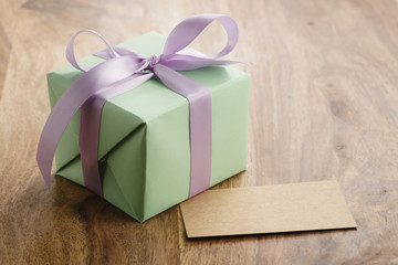 green paper gift box with purple ribbon bow and empty greeting card on old wood table