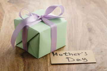 green paper gift box with purple ribbon bow and mothers day greeting card on old wood table