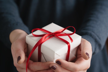 young female hands holding gift box with red ribbon