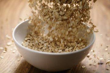 oat flakes fall in white bowl on wood table