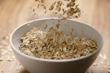 oat flakes fall in white bowl on wood table