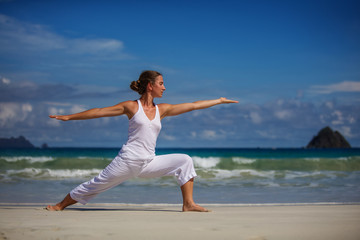 Caucasian woman practicing yoga at seashore of tropic ocean