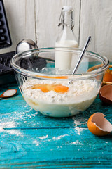 Making waffles at home - waffle iron, batter in bowl and ingredients - milk, eggs and flour.