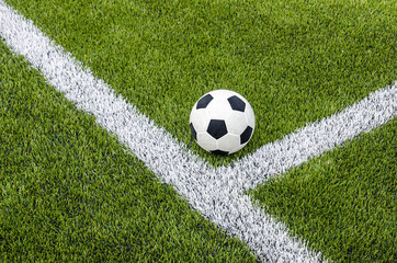 The soccer football on the white line in the artificial green grass field