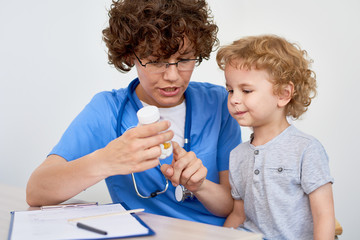 Portrait of young woman doctor showing can of pills and vitamins to adorable little boy