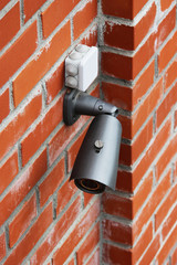 A video camera on a red brick wall protects the territory from the invasion of strangers.