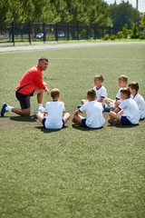 Fototapeta premium Portrait of boys sitting in front of coach on football field listening to pre game lecture