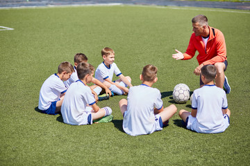 Naklejka premium Portrait of boys team sitting in front of coach on football field listening to pre game speech