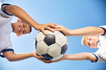 Low angle portrait of two boys in junior football team holding ball against  blue sky