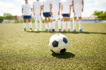 Closeup of football ball lying on field with blurred junior football team in background, preparing for game