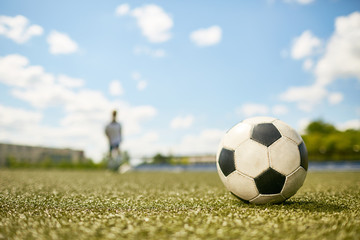 Closeup of football ball lying on green grass in field with figure of boy in background