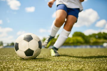 Low section portrait of unrecognizable teenage boy kicking ball during football practice in field