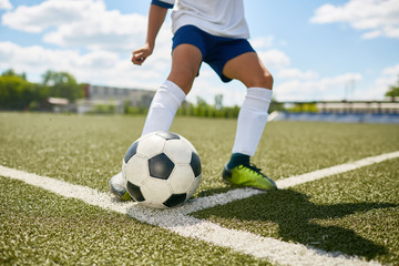 Closeup portrait of unrecognizable teenage boy kicking ball during football practice in field outdoors
