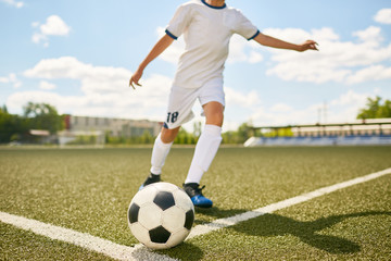 Portrait of unrecognizable teenage boy kicking ball during football practice in field outdoors