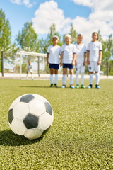 Obraz na płótnie Canvas Closeup of football ball lying on green grass with team in background