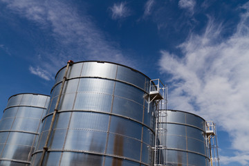 Slightly rusty steel storage tanks on a industrial site in Amsterdam, set against a blue summer sky with white clouds, The Netherlands.