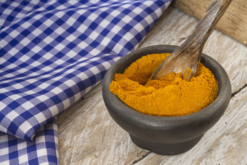 Turmeric powder in bowl and spoon on wooden table (curcuma longa)