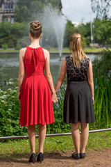Rückansicht von 2 Mädchen Hand in Hand im Park in festlichen Kleidern