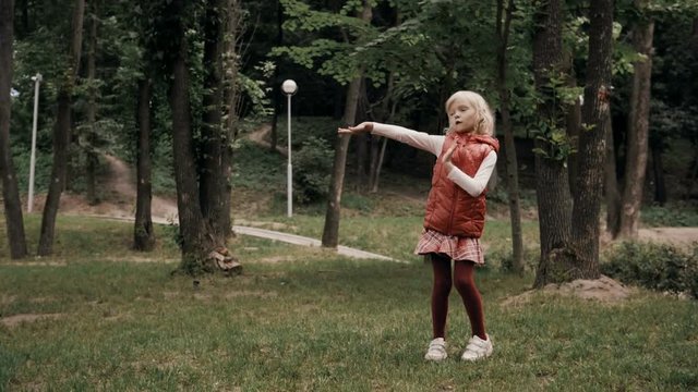 Little blond smiling cheerful girl dancing on a sunny day in a summer park. 4K