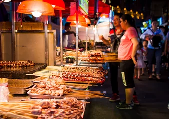 Zelfklevend Fotobehang NANNING, CHINA - JUNE 9, 2017: Food on the Zhongshan Snack Street, a food market in Nanning with many people bying food and walking around © creativefamily