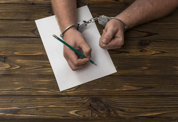 Men's hands with handcuffs fill the police record, confession. on top see the police investigative...