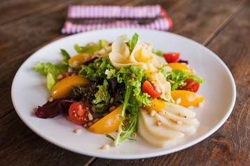 Green salad with cheese and fruits on plate. Lettuce, fresh vegetables decorated pine nuts, avocado, pearch and pear, serving in restaurant close up