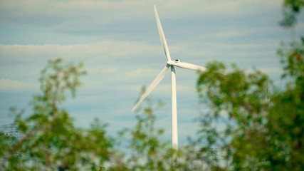 Wind generator behind waving green tree leaves