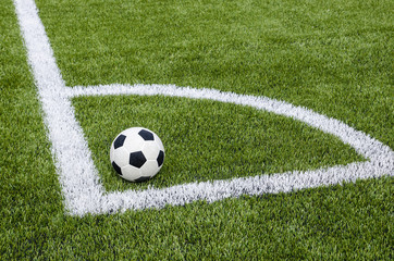 The soccer football in the corner on the artificial green grass field