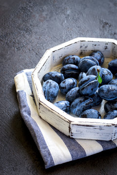 Dark blue plum in white tray on a black background closeup
