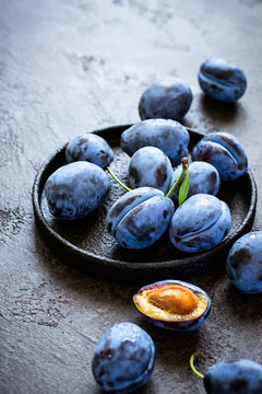 Dark blue plums in cast iron plate on black background closeup
