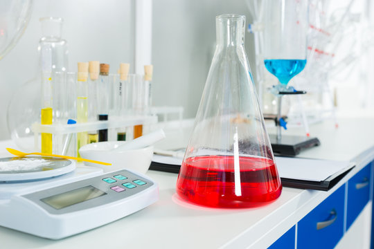 White powder on special scales near fask with red liquid for some research in a laboratory