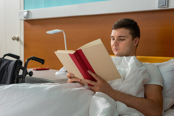 Portrait of male patient lying in the hospital bed and reading a book in hospital ward