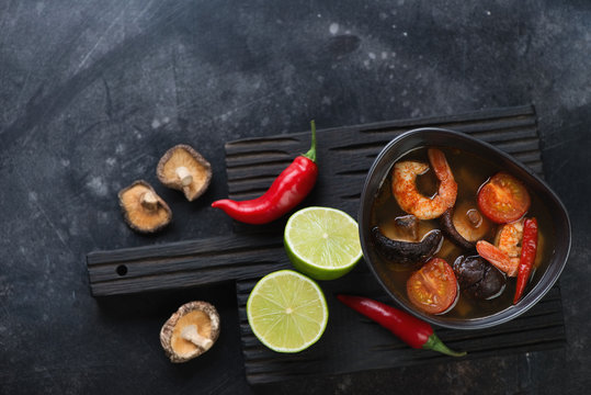 Hot Tom Yum soup with some of its cooking ingredients on a dark scratched metal background, flat-lay with space