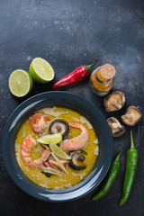 Thai green curry soup with addition of shrimps and shiitake mushrooms. Flat-lay with space on a dark metal surface