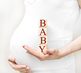Pregnant woman holding wooden cubes with word "Baby".