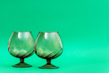 Two empty brandy glasses on a green background.