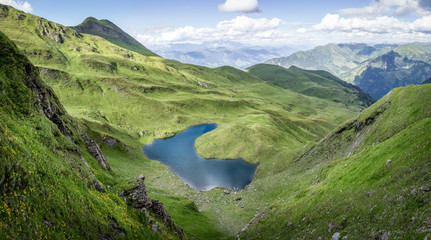 Fototapeta na wymiar Mountain landscape with green pastures and lake in the alps