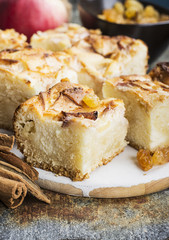 A simple homemade pie with apples and sour cream on a gray background with cinnamon sticks, an apple, caramel sweets. Top view. Selective focus.