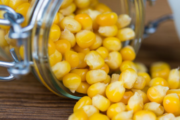 Detail of boiled corn spilled on wooden table. Tasty and healthy vegetarian snack in glass jar.