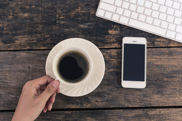 Close up of women's hands holding smart phone with  blank screen with hot coffee cup on wooden table top view.