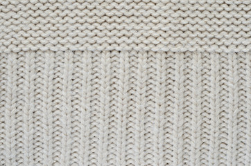Texture of a beige knitted sweater close-up. Vertically oriented pigtails on knitted fabric