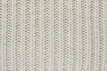 Texture of a beige knitted sweater close-up. Vertically oriented pigtails on knitted fabric. Uniform knitting pattern
