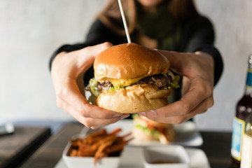 Frau isst Cheeseburger in einem Restaurant, sie hält das Sandwich in die Kamera
