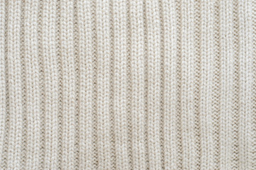 Texture of a beige knitted sweater close-up. Vertically oriented pigtails on knitted fabric....