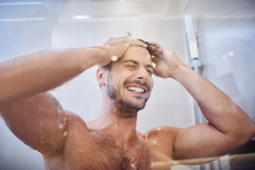 Cheerful well-built handsome young man laughing while in the shower