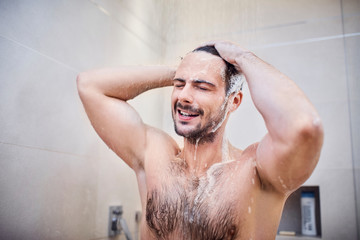 Handsome young man washing head with shampoo while taking a shower with closed eyes