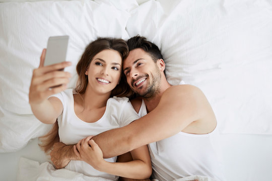 Cute loving couple taking selfie while lying in bed together