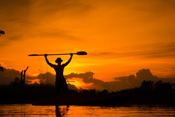 Silhouette of  fisherman standing on boat,hold paddle,on sunset background.