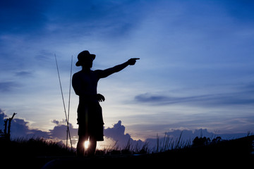 Silhouette of fisherman on the boat pointing with finger in sky.
